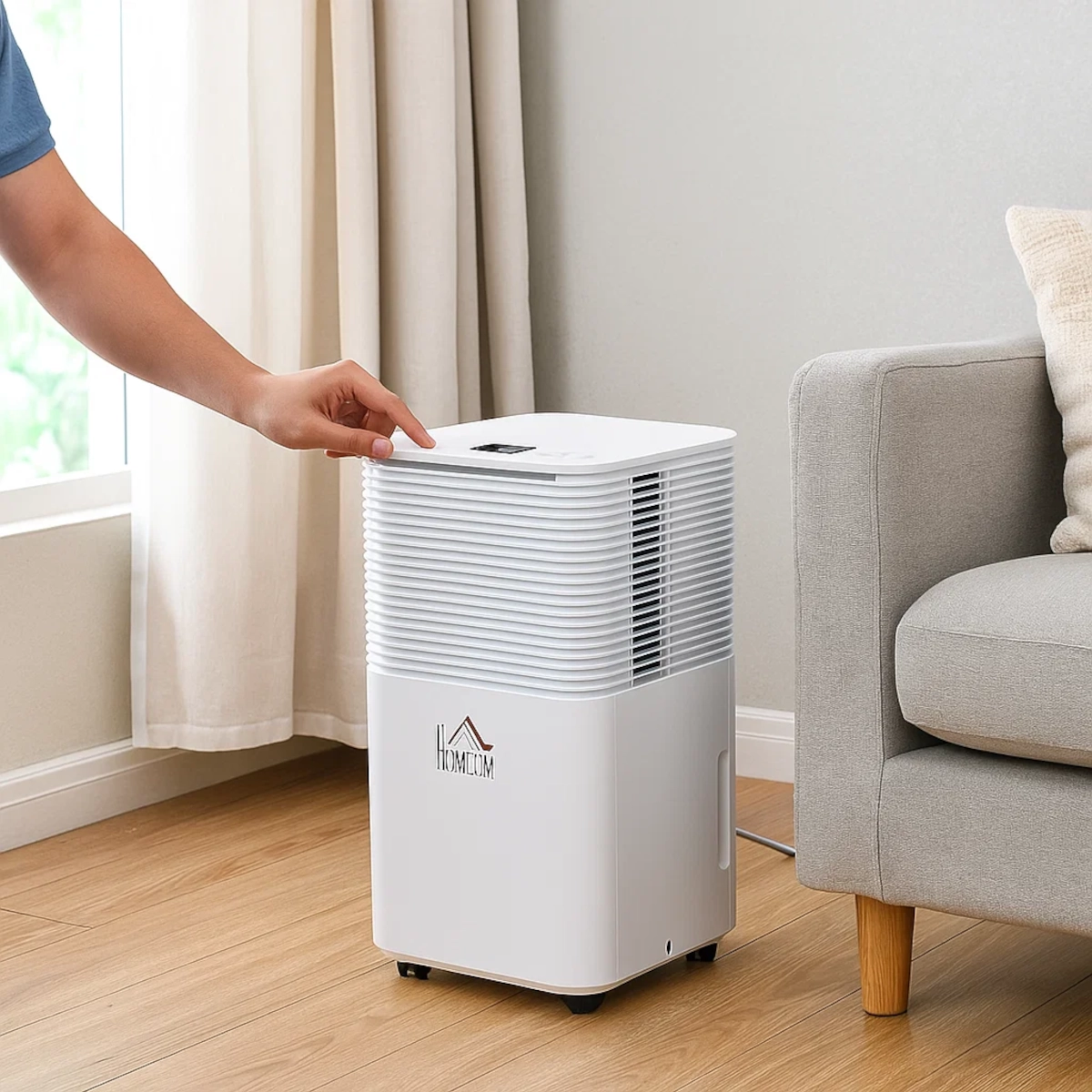 Person turning on HOMCOM dehumidifier placed beside a sofa in a bright living room.