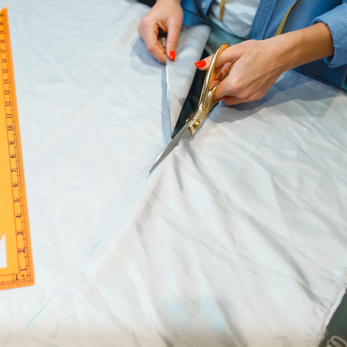 Close-up of scissors cutting light blue fabric along a chalk measurement line