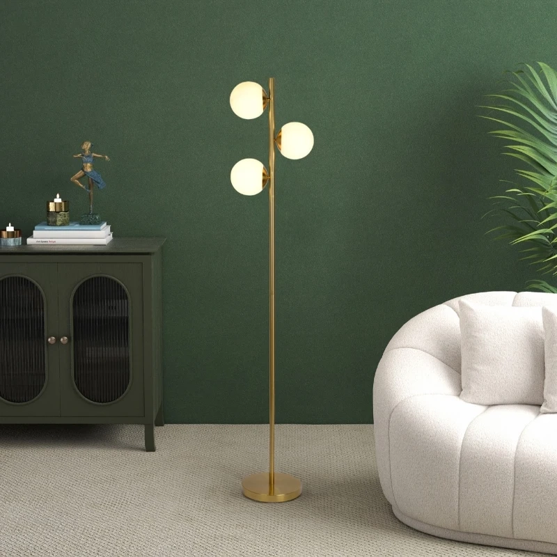 Stylish living room with gold floor lamp featuring three glowing opal glass shades against green wall.
