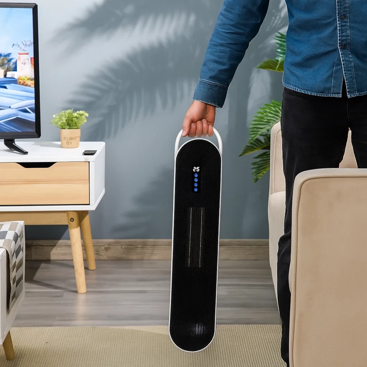 Person carrying slim ceramic tower heater by built-in handle in a living room.