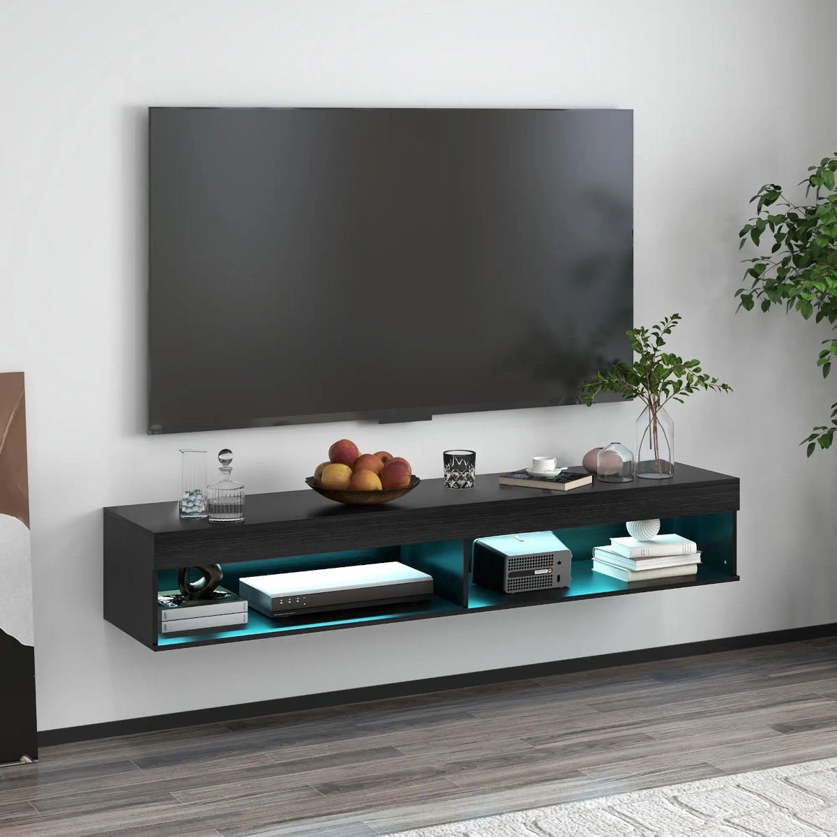 Floating black wall-mounted TV stand with blue-lit shelves, books, decor, and electronics beneath mounted TV.