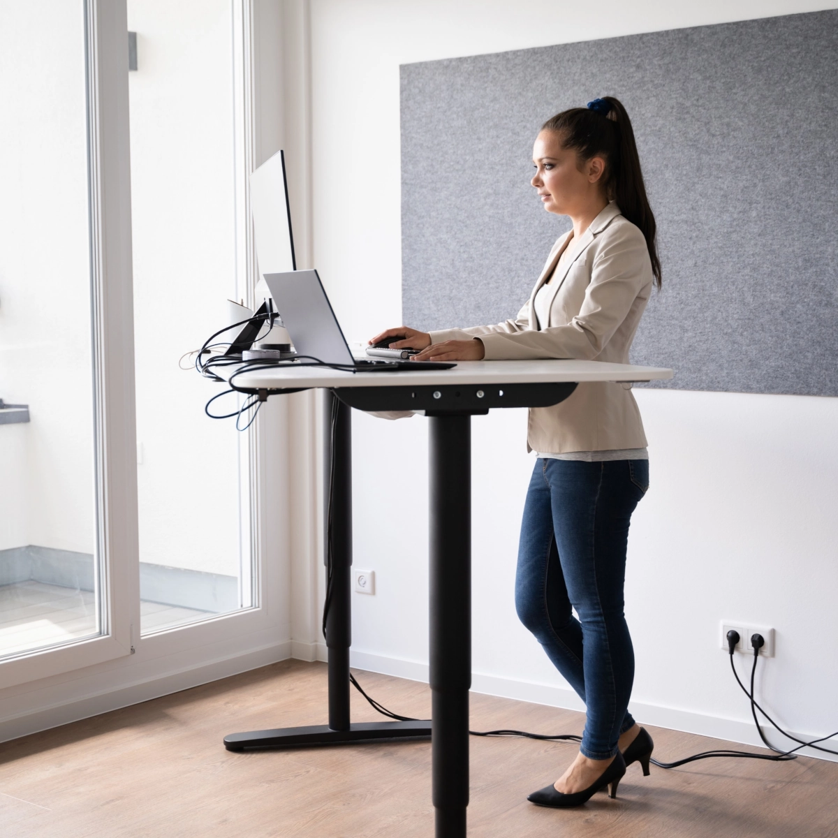 Woman working on laptop at adjustable standing desk.