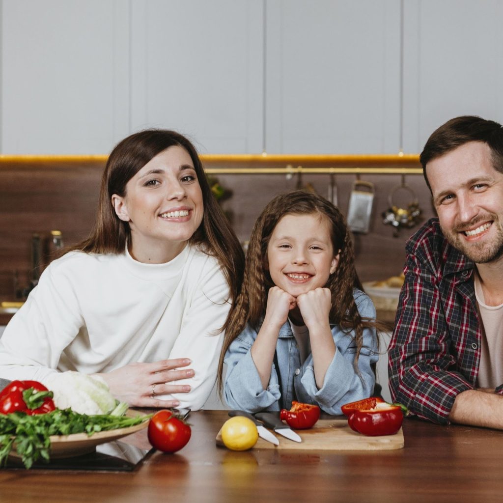 Smiling family gathered around kitchen island preparing and enjoying food together.