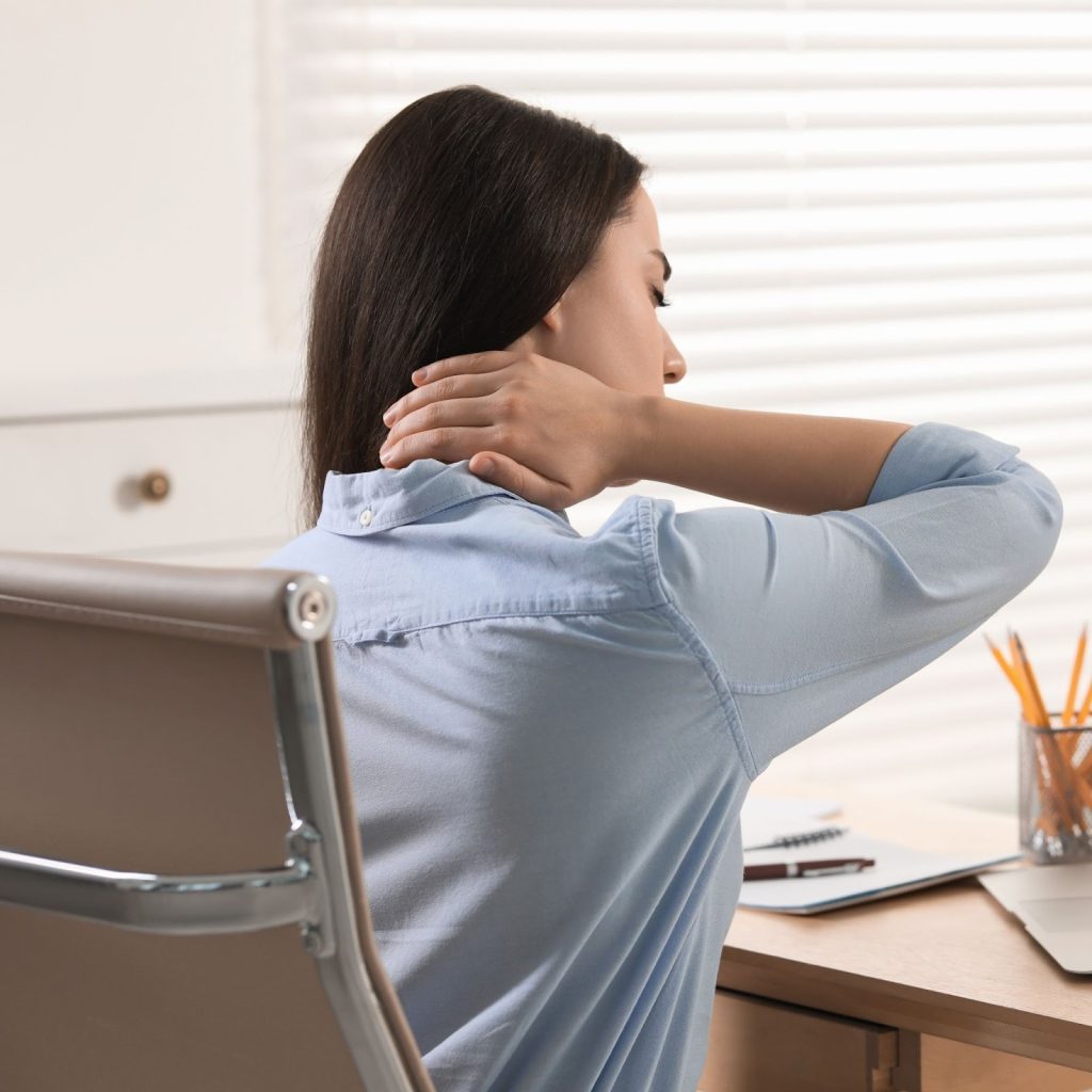 Woman seated at desk massaging neck after long computer session