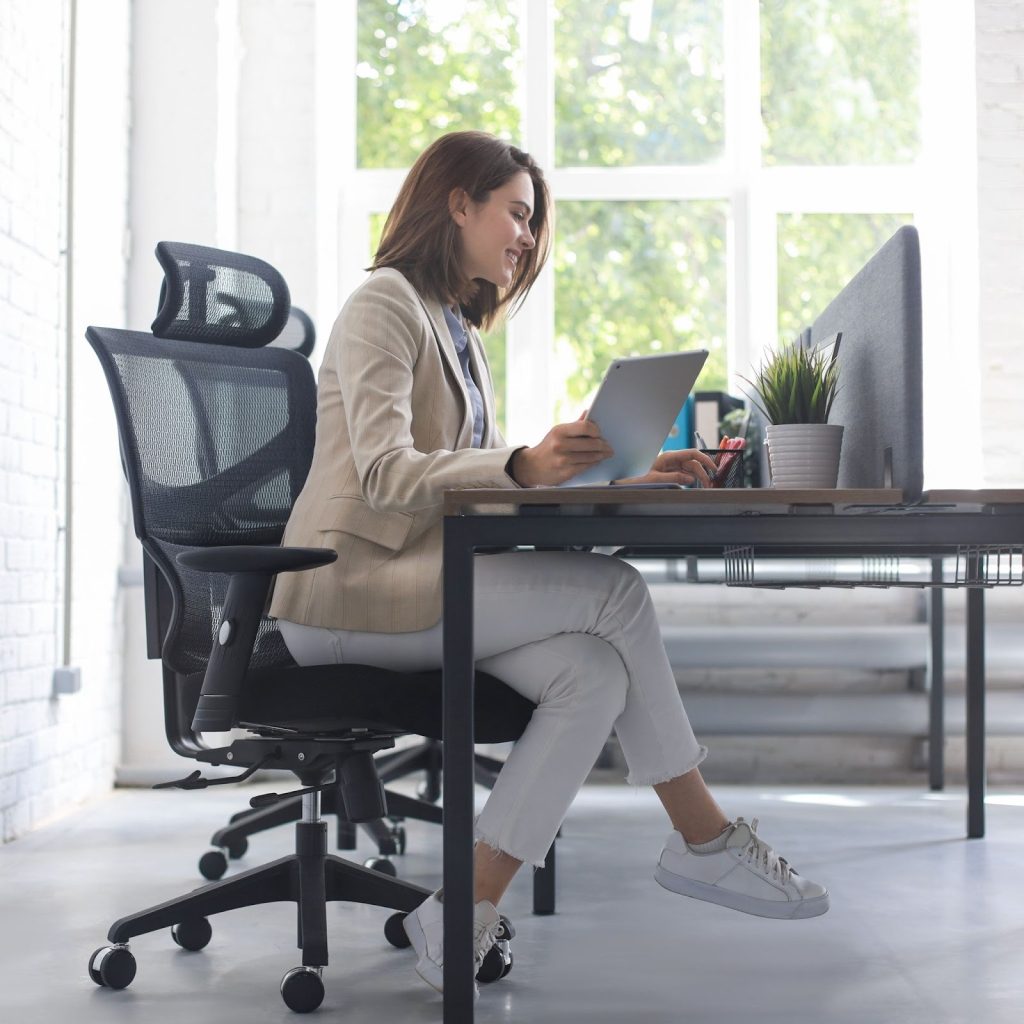 Woman working on tablet in bright office using ergonomic mesh chair