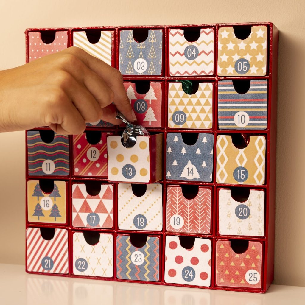 Hand opening numbered advent calendar drawer filled with wrapped chocolate treat.