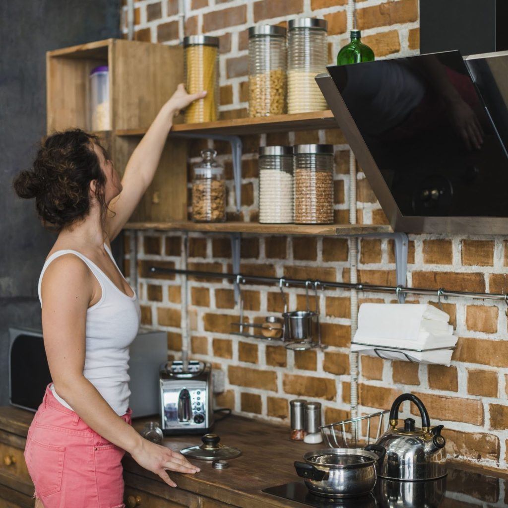 Woman organizing pasta jars on floating kitchen shelves using vertical wall space efficiently.