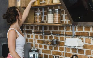 Woman organizing pasta jars on floating kitchen shelves using vertical wall space efficiently.