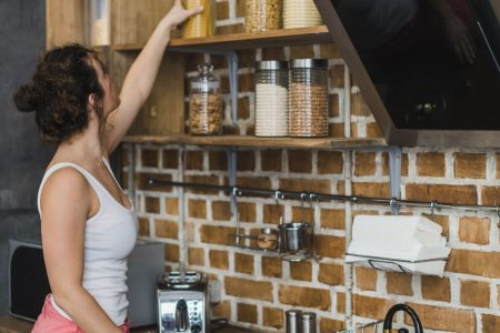 Woman organizing pasta jars on floating kitchen shelves using vertical wall space efficiently.