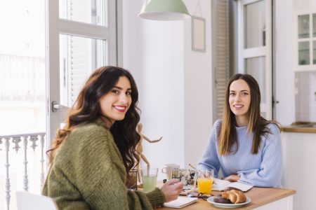 Two women enjoying breakfast at a small kitchen nook with natural light and modern decor.