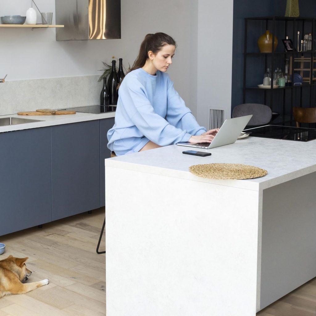  Woman using laptop at sleek kitchen island in modern minimalist home interior.