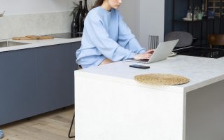 Woman using laptop at sleek kitchen island in modern minimalist home interior.