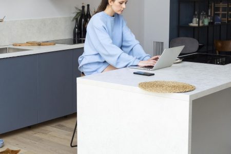 Woman using laptop at sleek kitchen island in modern minimalist home interior.