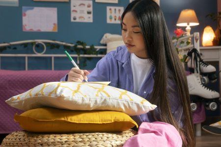 Student writing in colorful dorm room with cushions and décor.