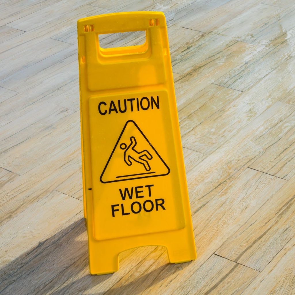 Wet floor caution sign placed on wooden floor to ensure cleaning safety.