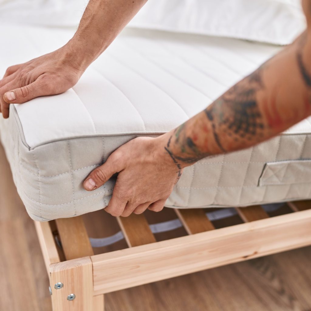 Person placing soft mattress on wooden bed frame for setup.