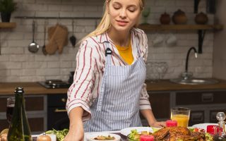 Woman preparing a festive buffet on a kitchen island with roasted vegetables, chicken, and table décor.