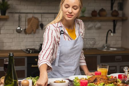 Woman preparing a festive buffet on a kitchen island with roasted vegetables, chicken, and table décor.