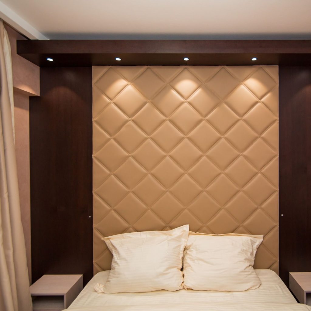 Luxurious tan quilted wall headboard with built-in lighting and dark wood framing.