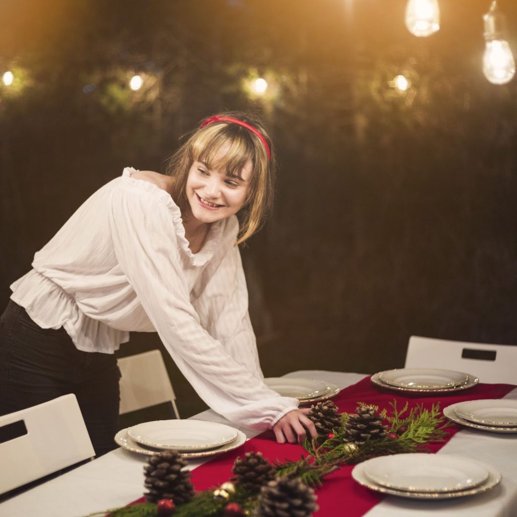 Woman arranging pinecone centrepiece on Christmas dining table with festive lights