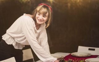 Woman arranging pinecone centrepiece on Christmas dining table with festive lights