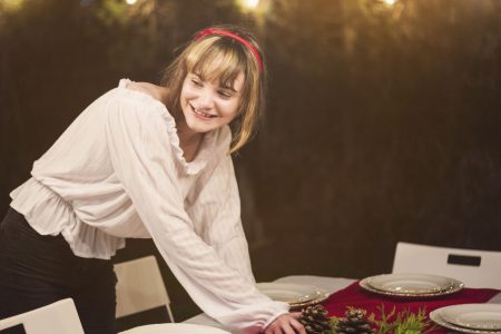 Woman arranging pinecone centrepiece on Christmas dining table with festive lights