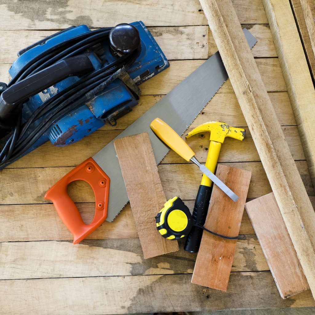 DIY dog gate tools including saw, hammer, chisel, and wood pieces arranged on a workbench.